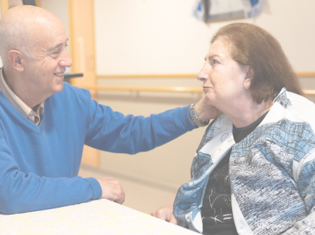 Persona acompañando a otra en un espacio interior, sentadas frente a una mesa con planta decorativa. Imagen que representa acompañamiento en demencia, cuidados personalizados y atención centrada en la persona, destacando ética del cuidado y respeto a los